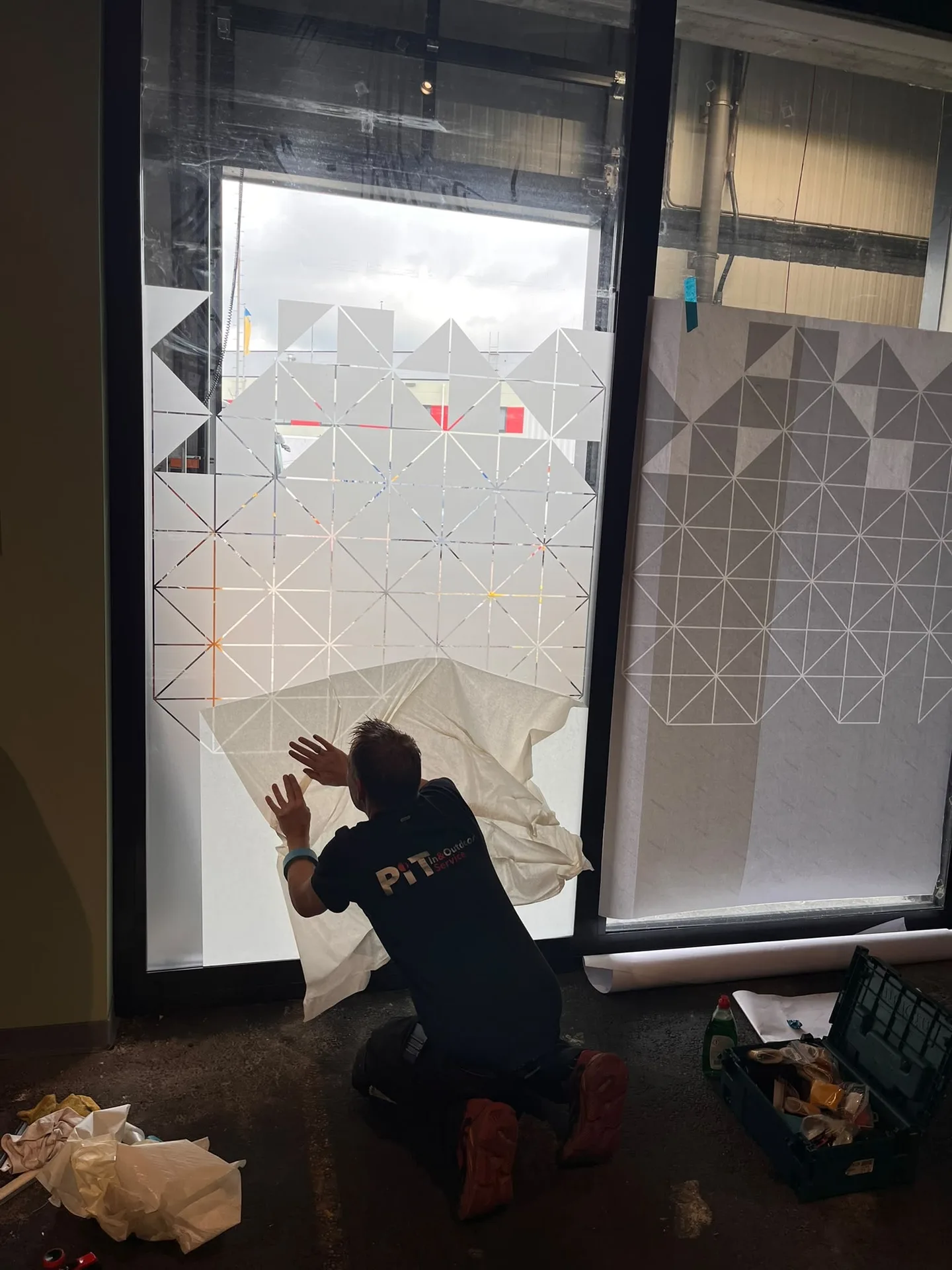 PIT-monteur brengt decoratieve raamfolie met een geometrisch patroon aan op een raam.